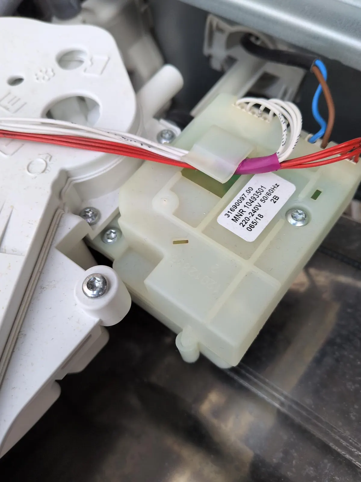 Dystrybutor wody pralki Miele z etykietą części, zamontowany przy dozowniku